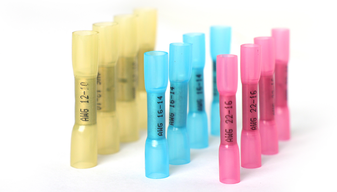 Assorted yellow, blue and pink butt wire connector sleeves standing upright, grouped by AWG size for quick selection