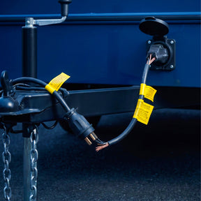 Damaged trailer wiring cable with exposed copper strands beside a hitch, safety chains and exterior power socket.