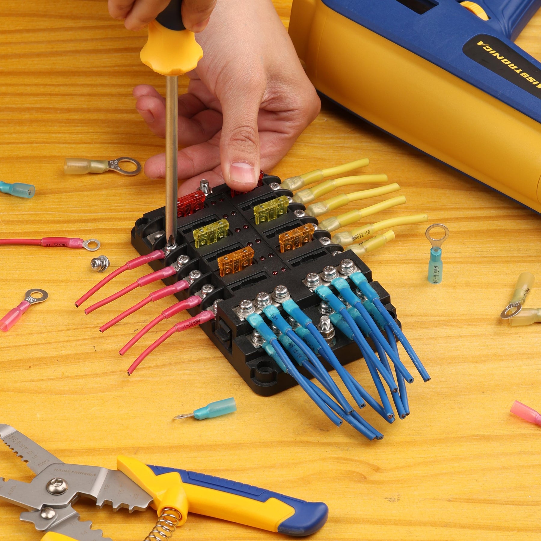 Technician tightens a fuse panel; colored leads with ring and fork lugs use heat shrink for wires on a wooden workbench.