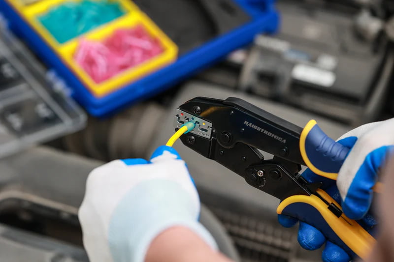 Studio shot of yellow blue handle ratchet crimping tool by Haisstronica with adjustable wheel and AWG scale on jaws