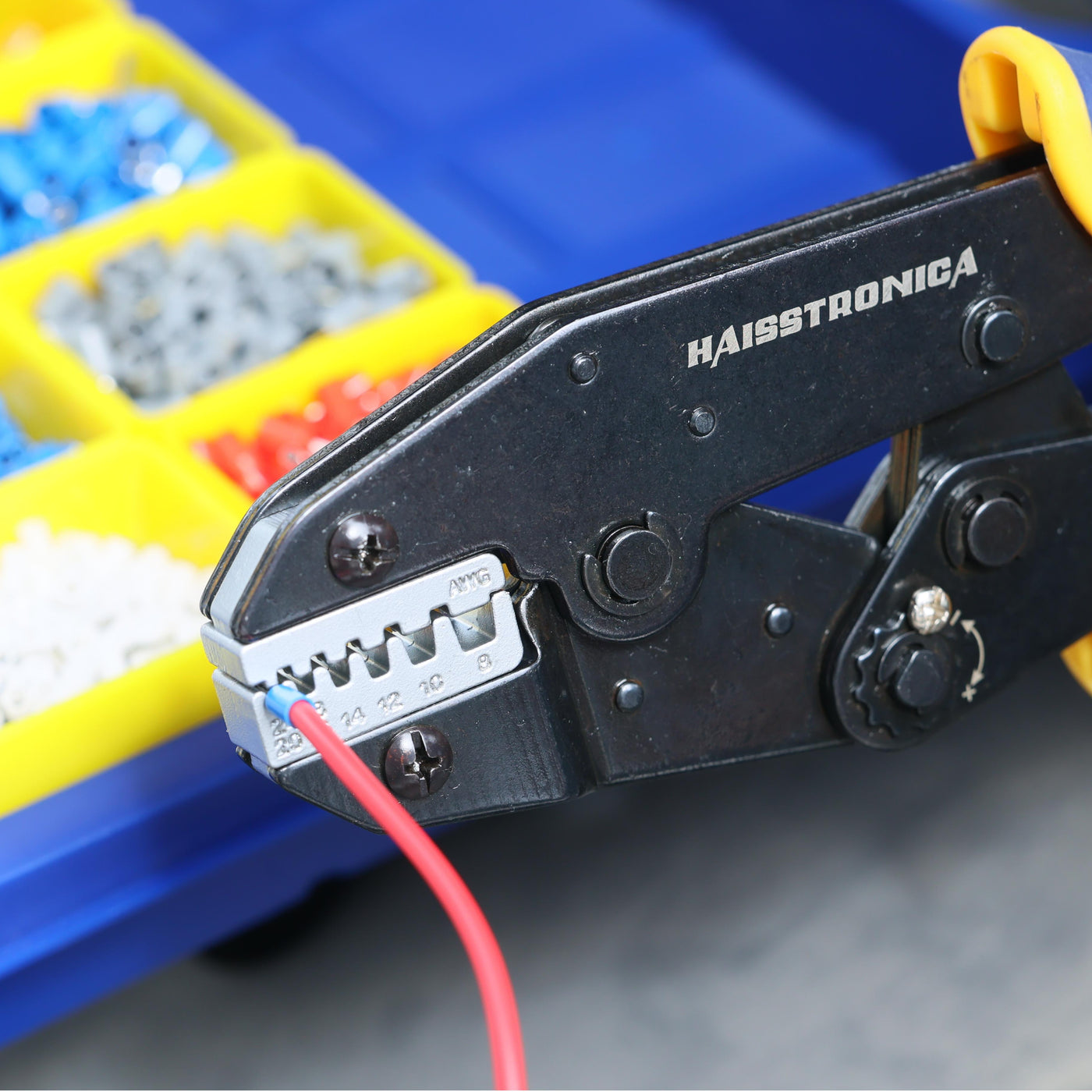 haisstronica applying a crimp on butt connector; AWG scale on die visible as yellow trays nearby hold assorted terminals